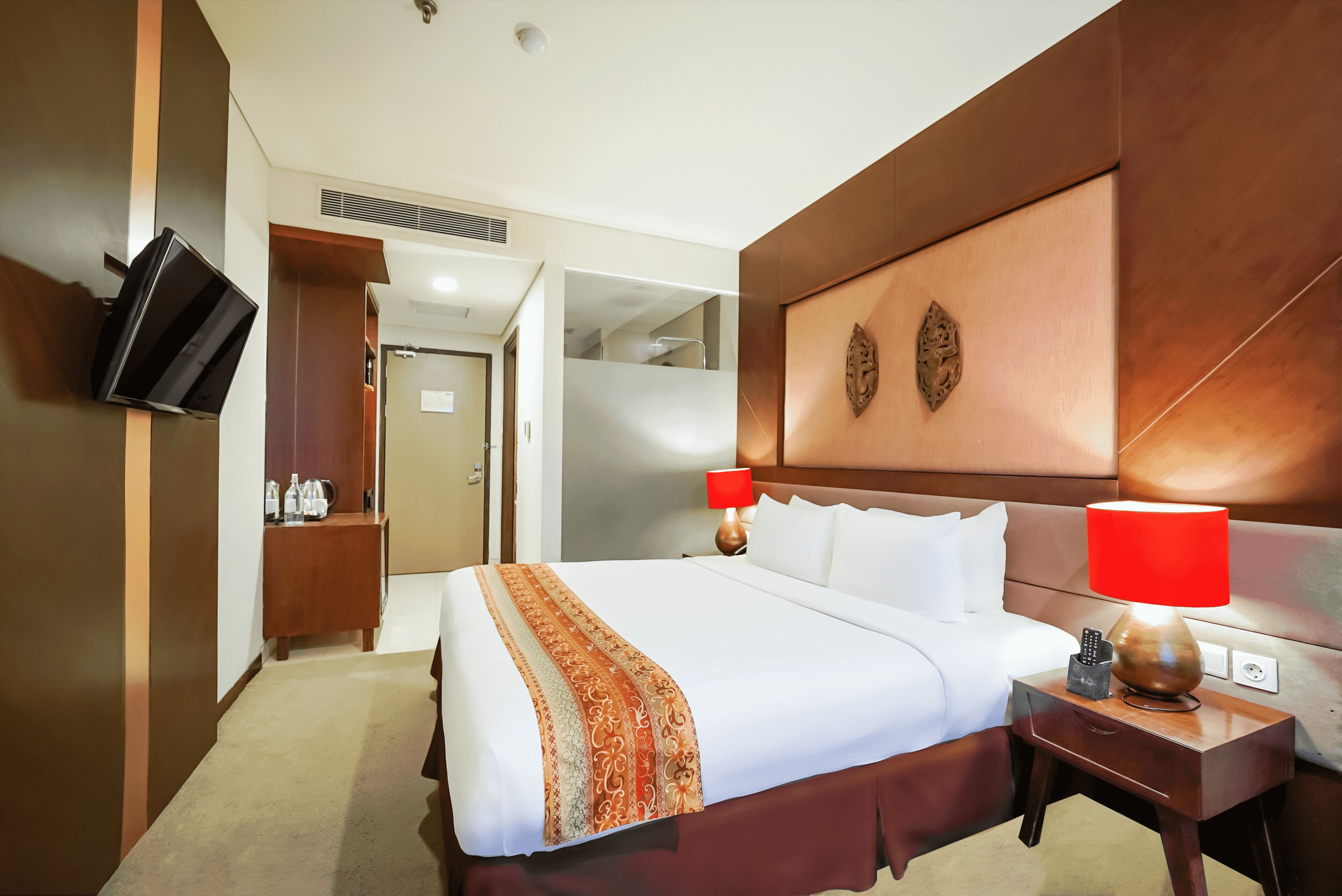 A hotel room with a large bed, two bedside lamps, a wooden nightstand, a TV mounted on the wall, and a mirror above the bed.