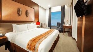 Ein Hotelzimmer mit einem großen Bett, einem Schreibtisch, einem Sessel, einem Fernseher und Blick ins Freie.