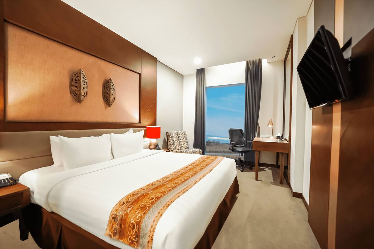 Ein Hotelzimmer mit einem großen Bett, einem Schreibtisch, einem Sessel, einem Fernseher und Blick ins Freie.