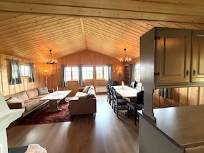 A spacious room with a high wooden ceiling, a dining table with chairs, a sofa, and a fireplace. - Torsetlia Fjellstue og Hyttegrend (Nore og Uvdal)
