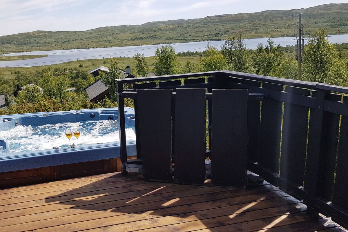 Ett trädäck med ett bubbelbad och utsikt över en sjö och kullar.