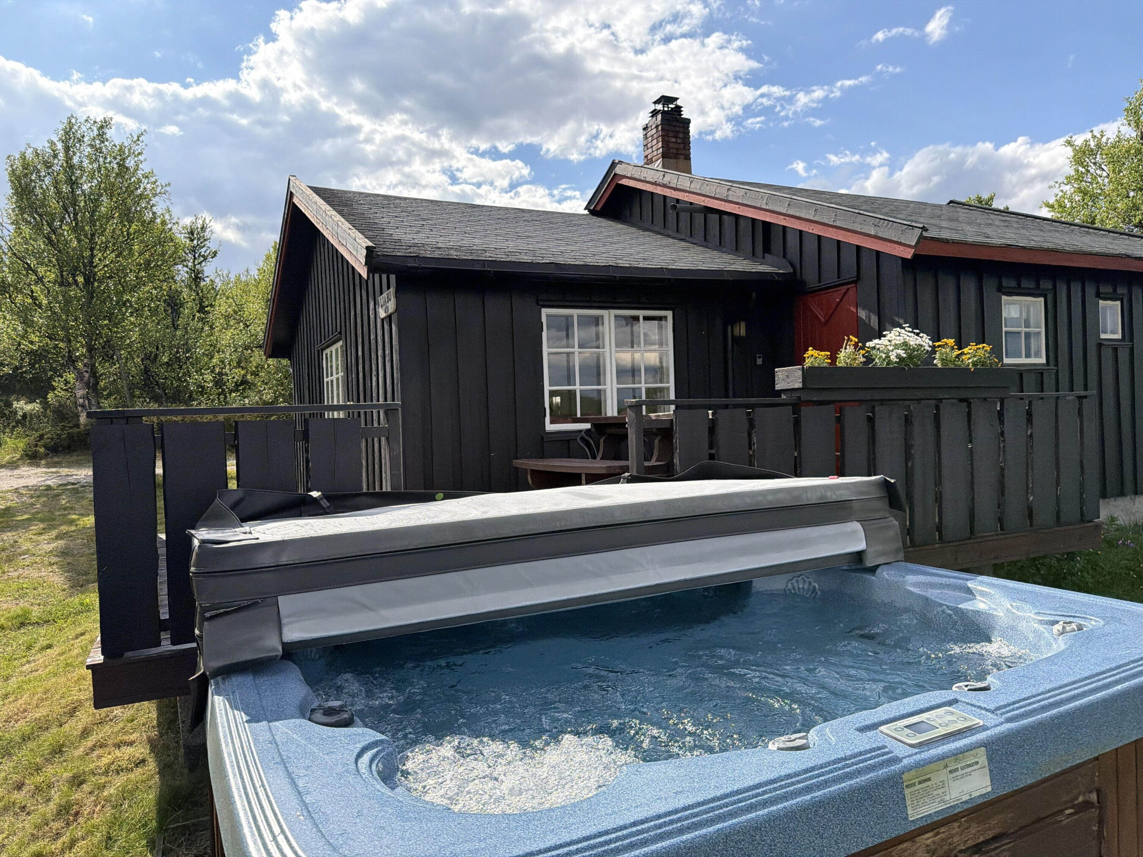 Un jacuzzi con cubierta de madera, una casa con chimenea y un patio cercado.