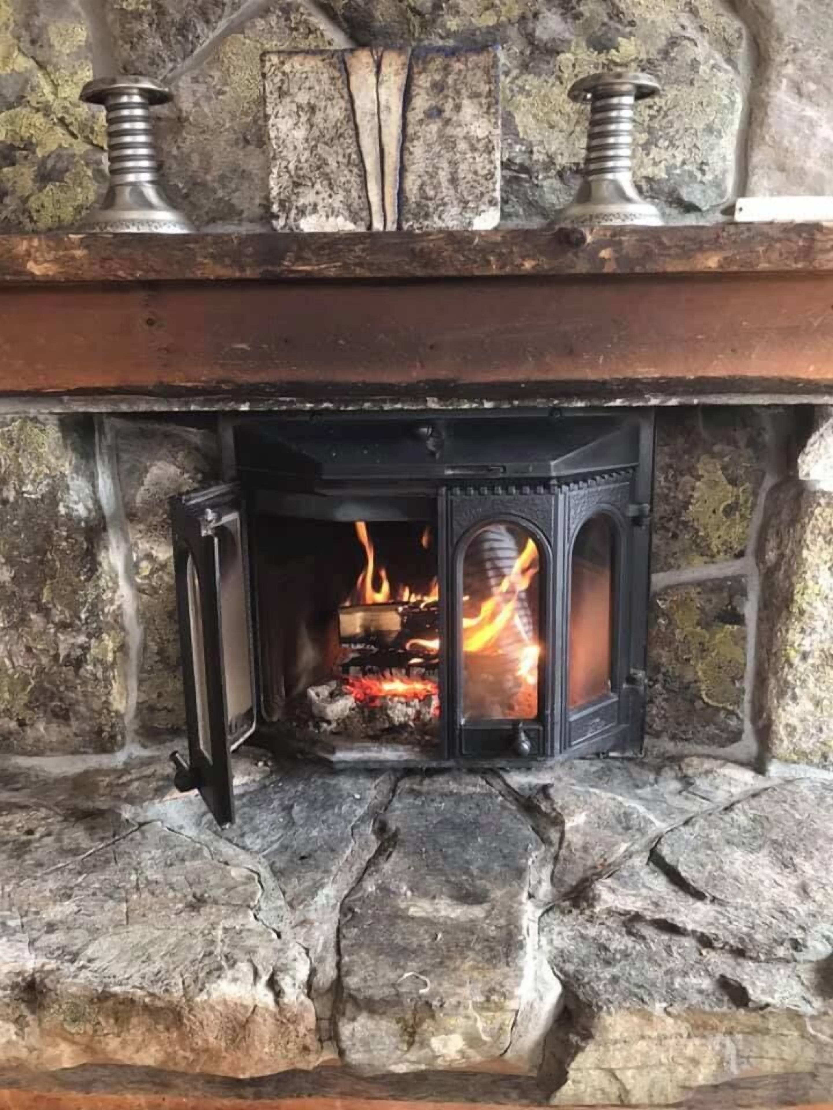 A stone fireplace with a black metal grate and a fire burning inside.