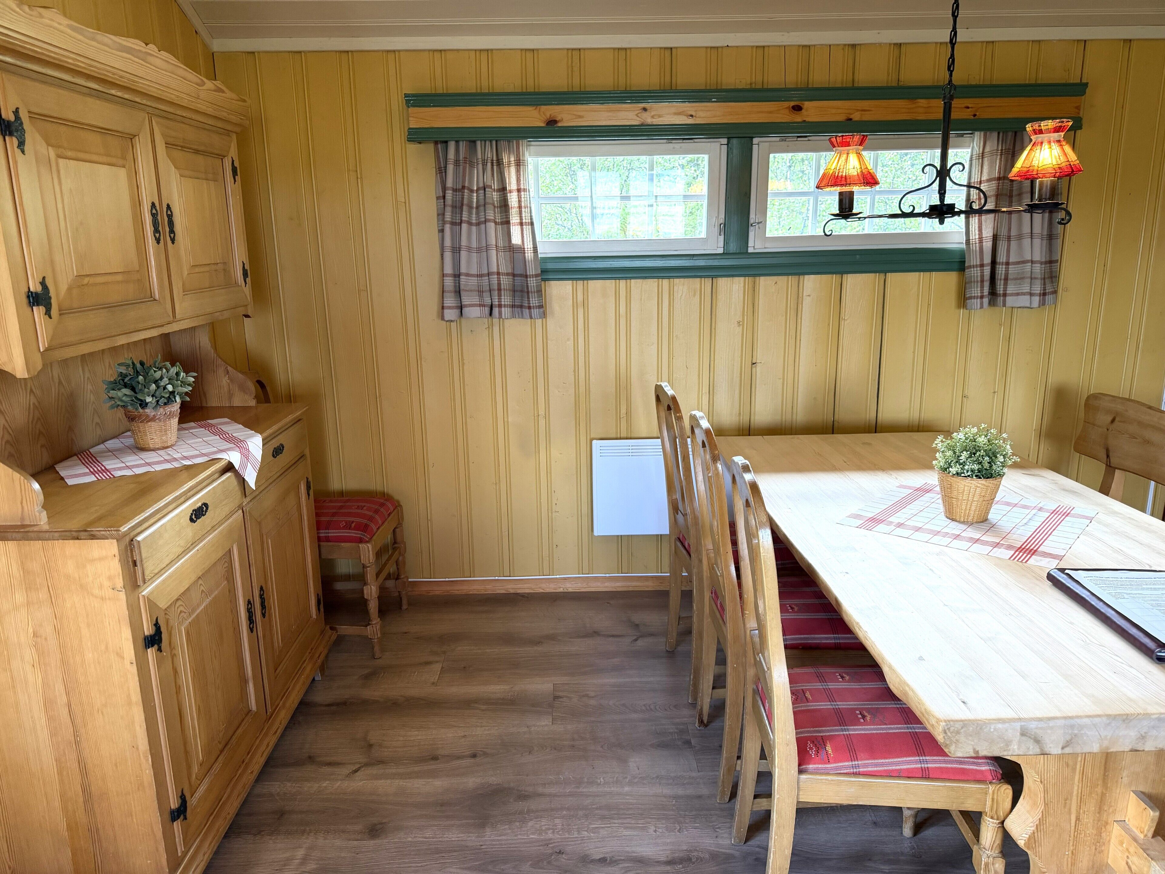 Comedor de madera con mesa, sillas y ventana con cortinas.