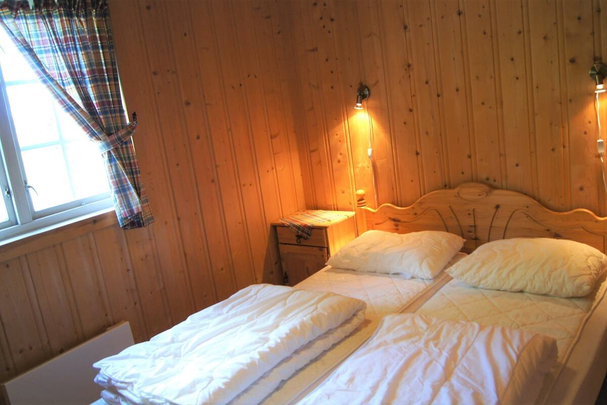Ett rum med träpanel, en säng, två sängbord och ett fönster med gardiner.