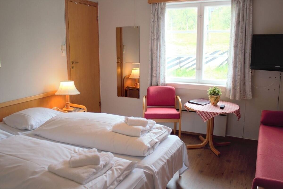 Ett hotellrum med två sängar, ett skrivbord, en stol, en tv och ett fönster med utsikt över en bro.