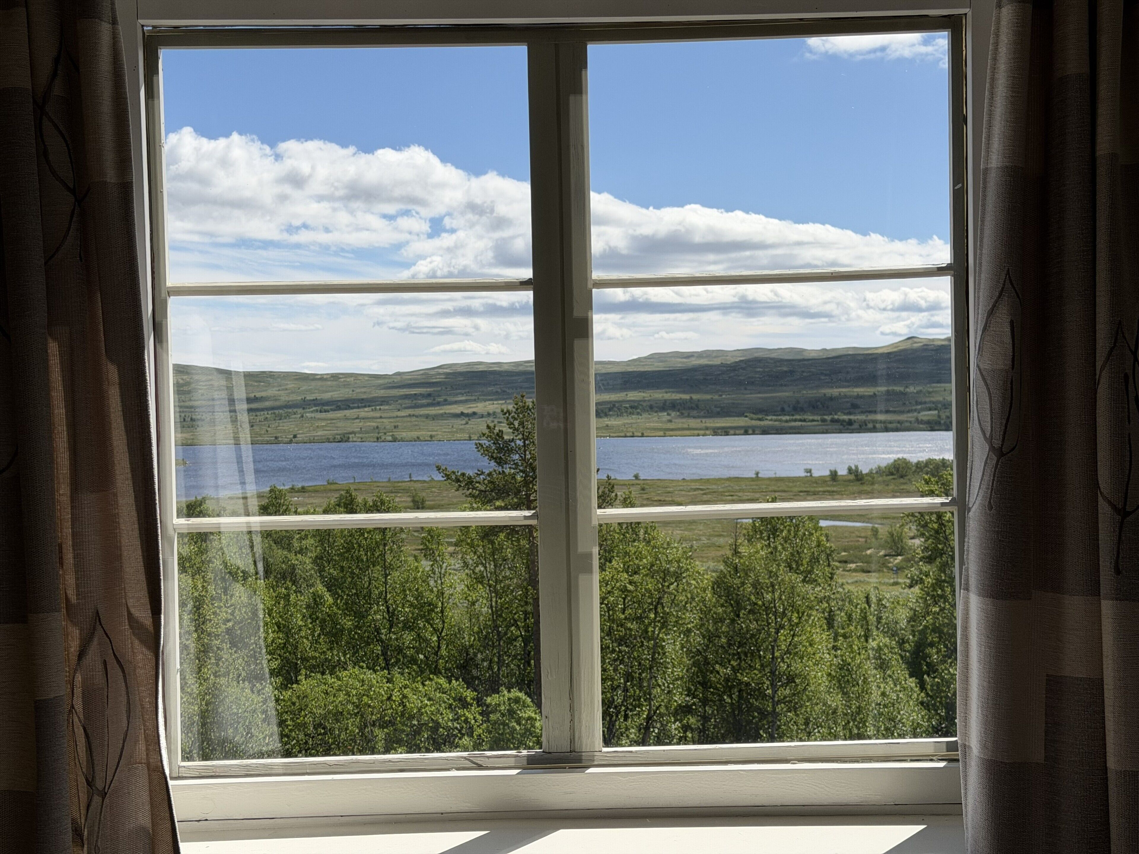 Ein Fenster mit Blick auf einen See und Hügel.