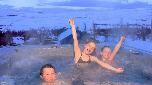 A hot tub with three people in it, surrounded by a snowy landscape and a house in the background. - Torsetlia Fjellstue og Hyttegrend (Nore og Uvdal)