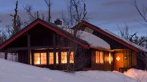 A wooden cabin with a sloped roof, large windows, and a snow-covered landscape at dusk. - Torsetlia Fjellstue og Hyttegrend (Nore og Uvdal)