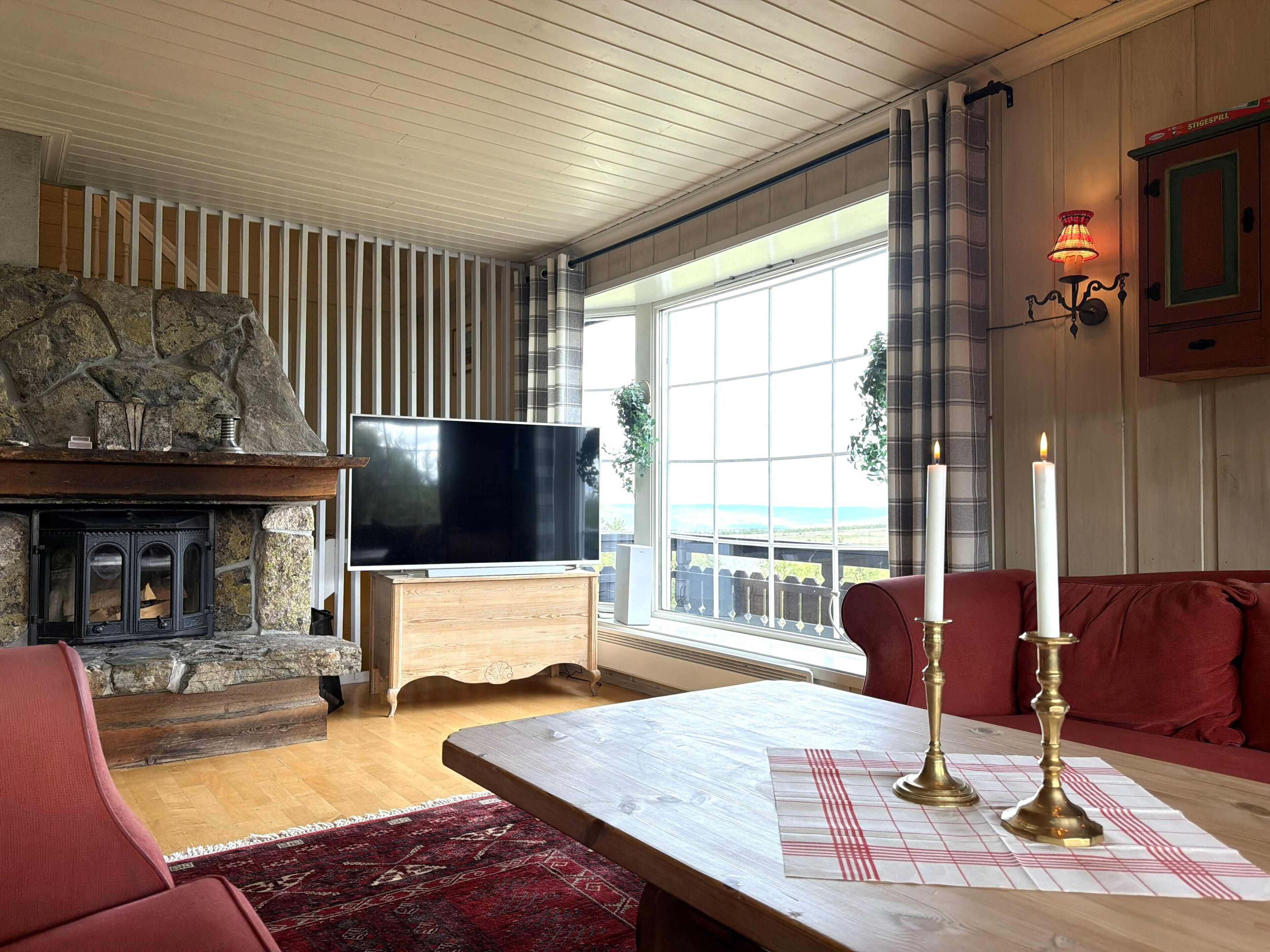 Ein gemütliches Wohnzimmer mit Kamin aus Stein, einem Flachbildfernseher, einem Couchtisch aus Holz und einem roten Sofa.