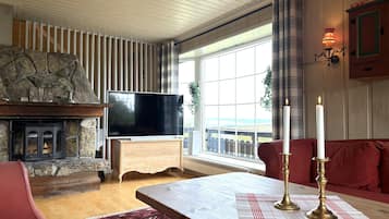 Ein gemütliches Wohnzimmer mit Kamin aus Stein, einem Flachbildfernseher, einem Couchtisch aus Holz und einem roten Sofa.