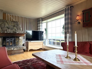 Una sala de estar acogedora con chimenea de piedra, televisor de pantalla plana, una mesa de centro de madera y un sofá rojo.