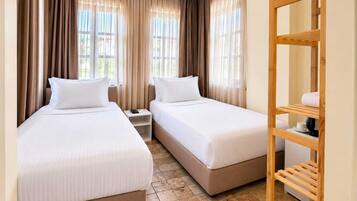 Una habitación de hotel con dos camas, un estante de madera y una ventana con cortinas.
