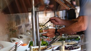 A person serving food at a buffet with various dishes and utensils.