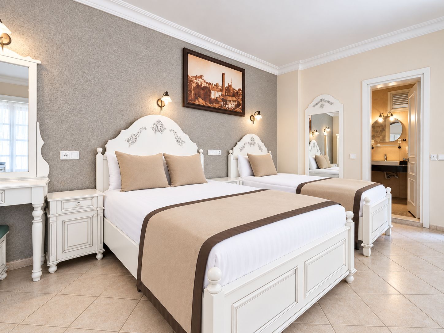 A hotel room with two beds, a large mirror, a painting on the wall, and a bathroom visible through an open door.