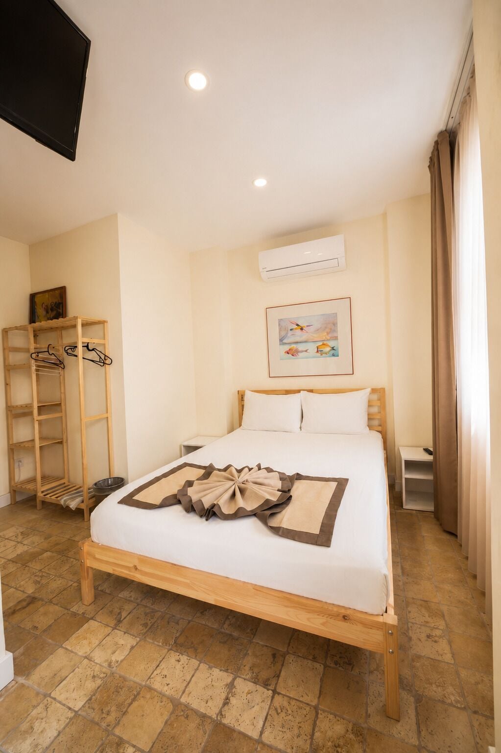 Habitación de hotel con una cama, un estante de madera, un equipo de aire acondicionado y un cuadro en la pared.