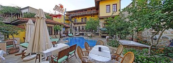Un espace aménagé au bord de la piscine, avec des chaises longues, une table et un jacuzzi, le tout entouré de bâtiments en pierre dotés de balcons.