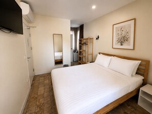 Habitación de hotel con una cama grande, un televisor de pantalla plana montado en la pared, un cabecero de madera y una obra enmarcada sobre la cama.