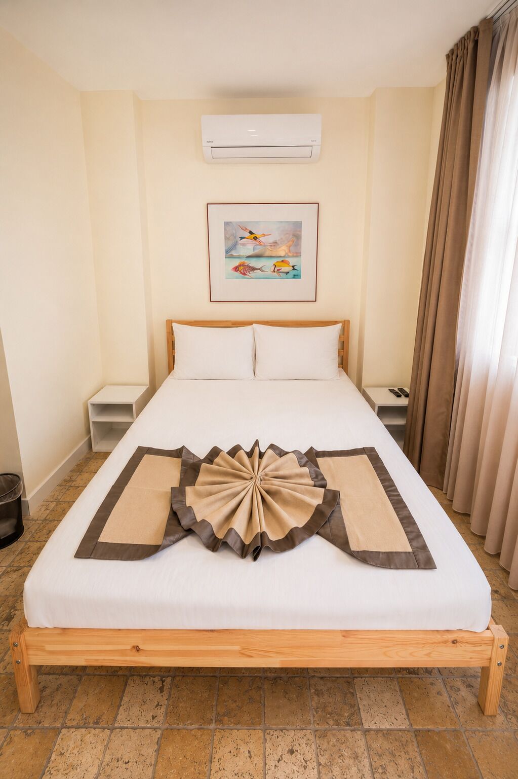 Hotelkamer met een bed, een airconditioner, een ingelijst beeld aan de muur en een gordijn voor het raam.