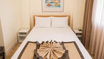 Quarto de hotel com cama, ar condicionado, quadro pendurado na parede e cortina na janela.