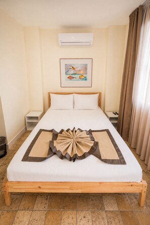 Una habitación de hotel con una cama, un equipo de aire acondicionado, un cuadro en la pared y una cortina en la ventana.