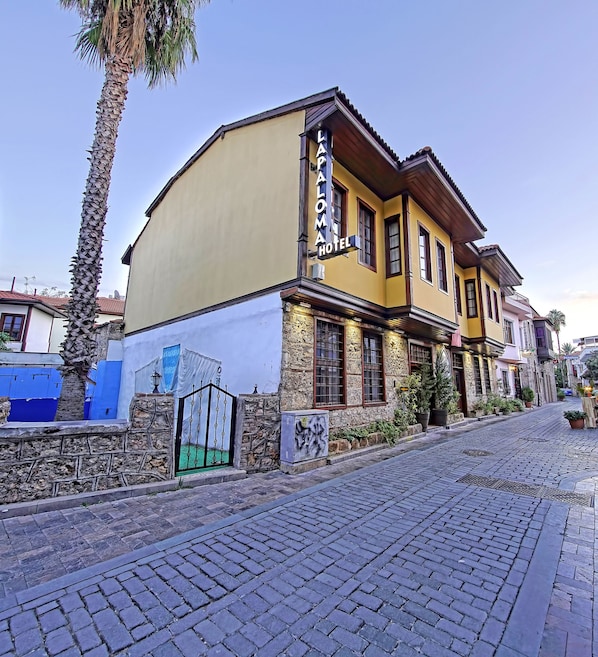 A hotel with a yellow facade, stone walls, and a cobblestone street. - La Paloma Hotel (Antalya)