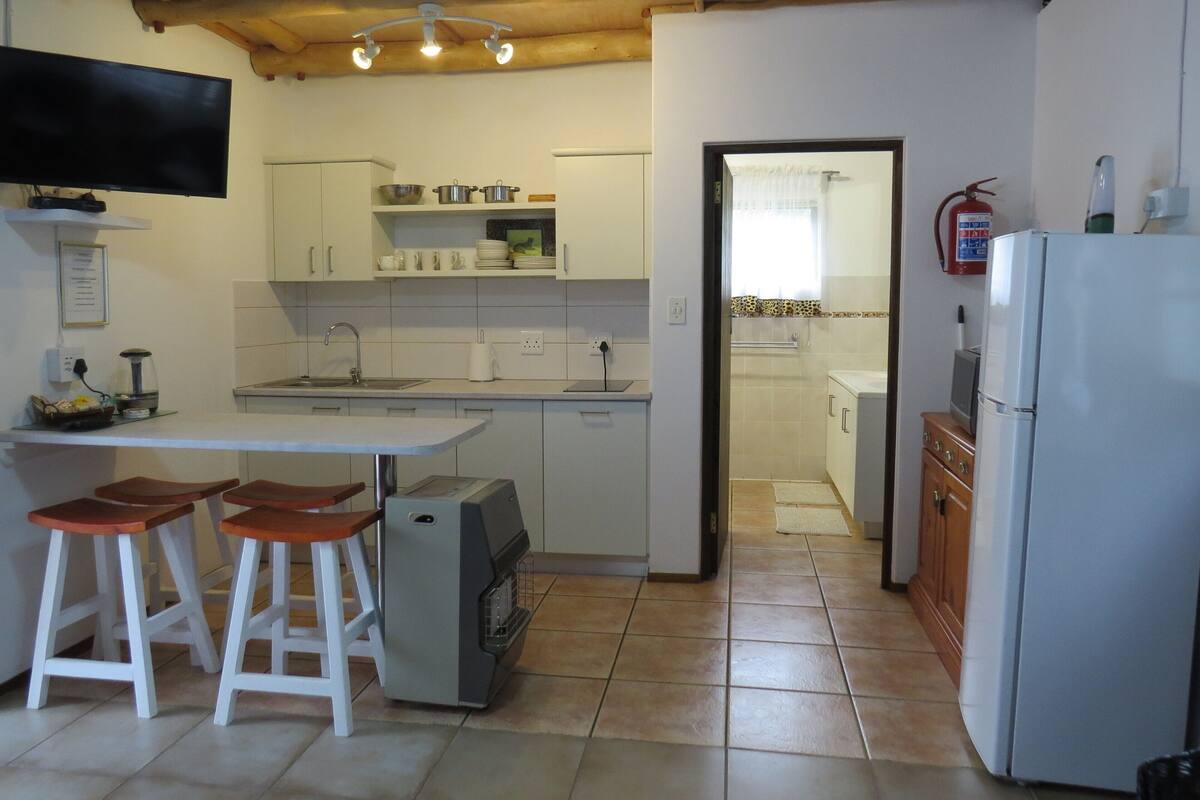 A compact kitchen with white cabinets, a built-in oven, a refrigerator, and a small dining area with stools.