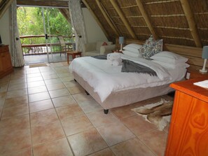 Un dormitorio con cama, mesita de noche de madera, una silla y vistas al verdor exterior.