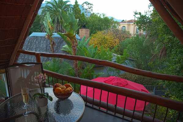 Un balcon avec une table en verre, un parasol rouge et un saladier rempli de fruits.