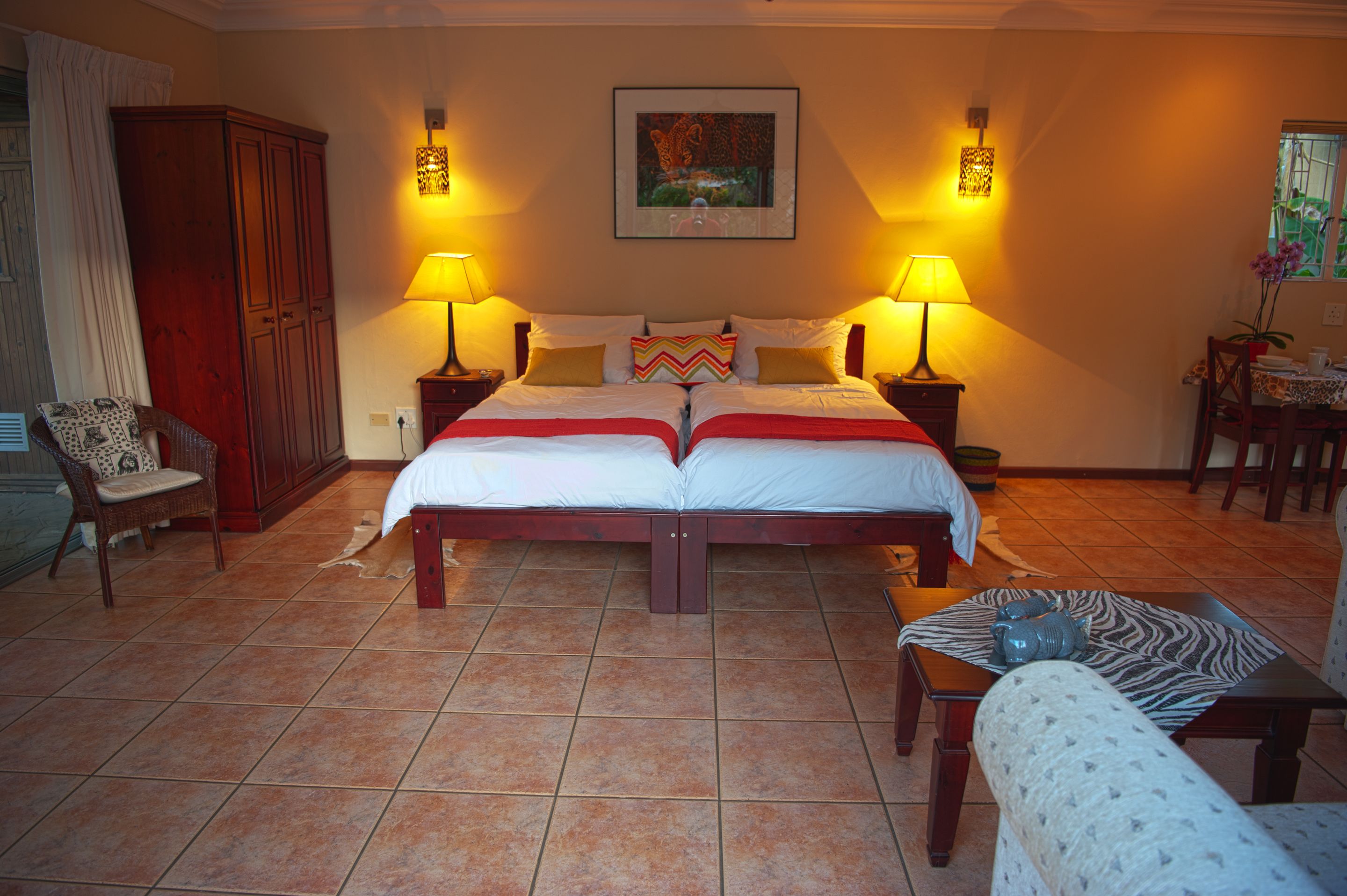 A double bed with two nightstands, a chair, a table with a vase, and a painting on the wall.