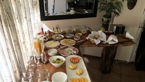A buffet table with various food items and drinks, including fruits, cheeses, and meats, arranged on a wooden table with a mirror and decorative items in the background. - Easy Five (Cape Town)