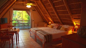 A cozy bedroom with a large bed, a desk, and a chair, a balcony with a table and chairs, and a thatched roof ceiling. - Easy Five (Cape Town)