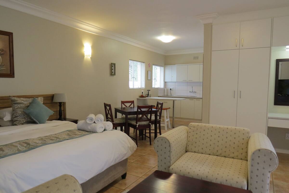 A bedroom with a bed, bedside table, lamp, and a small table with rolled towels.