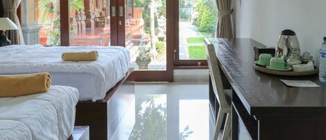 Habitación de hotel con dos camas, zona de comedor con mesa y sillas, y vista a un jardín a través de puertas de cristal amplias.