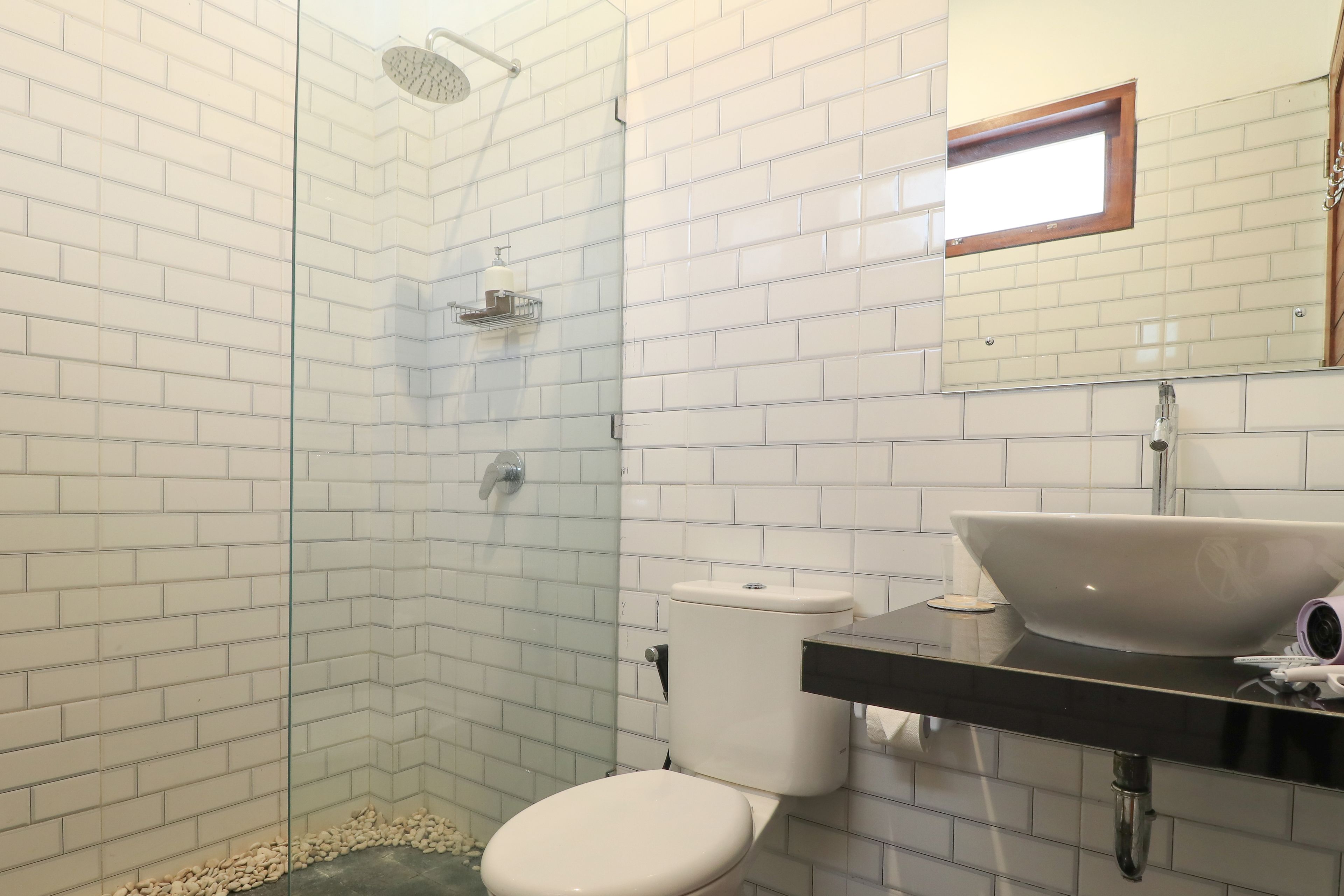 A bathroom with white tiled walls, a glass shower enclosure, a white toilet, and a black countertop with a white sink.