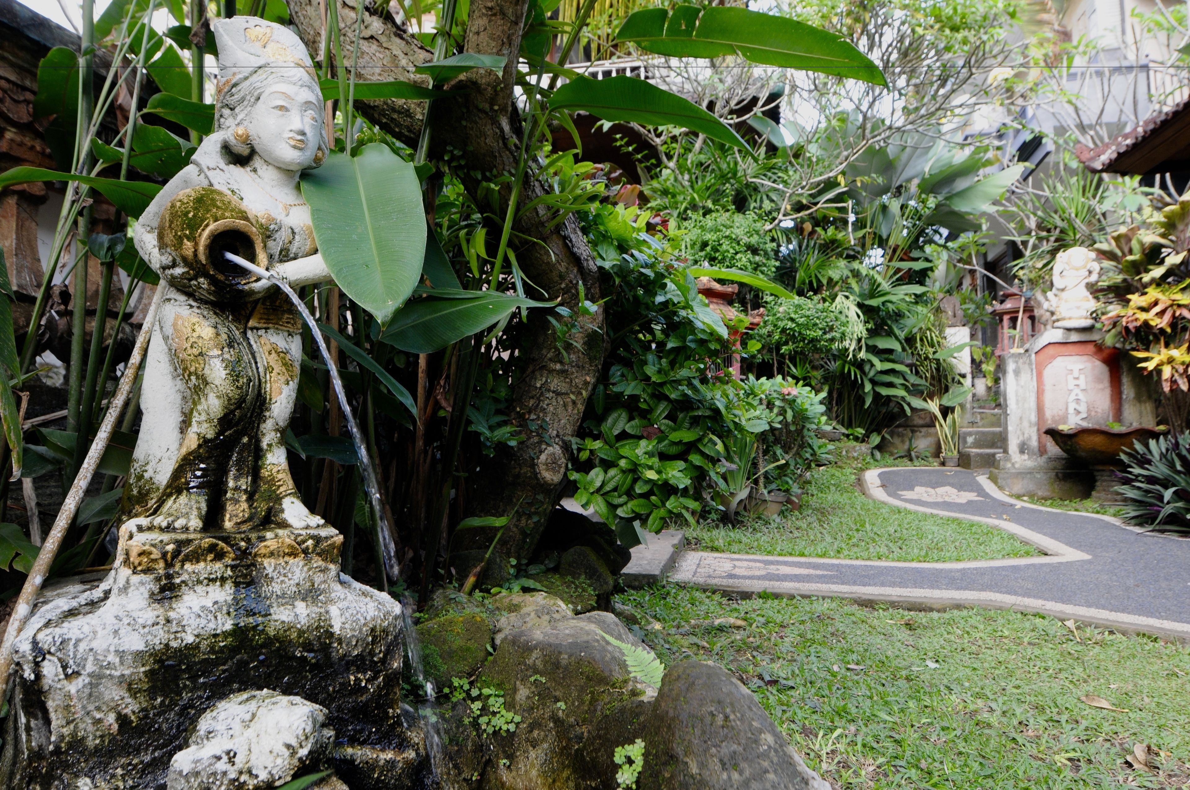 A garden with a stone statue, lush greenery, and a winding path.