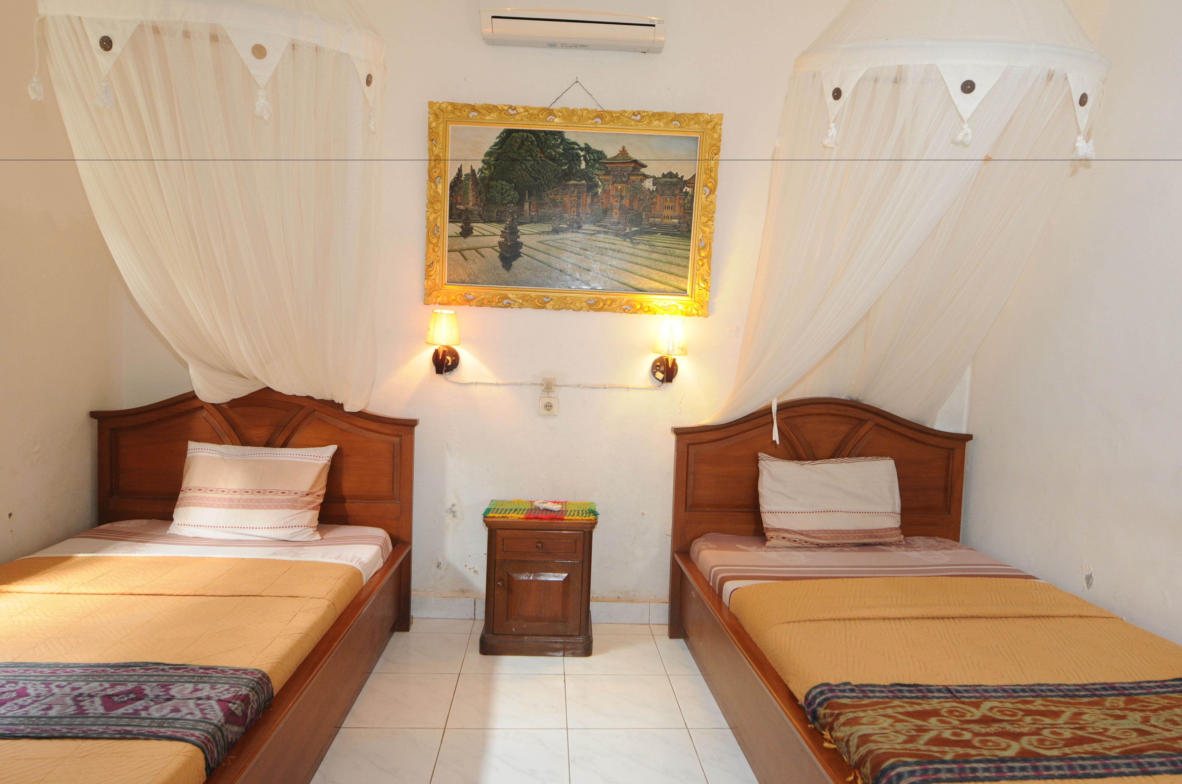 A room with two beds, a nightstand, a wall-mounted air conditioner, and a painting above the beds.