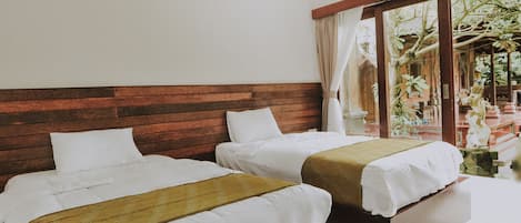 A hotel room with two beds, wooden headboards, white bedding, and a view of a garden through a glass door.