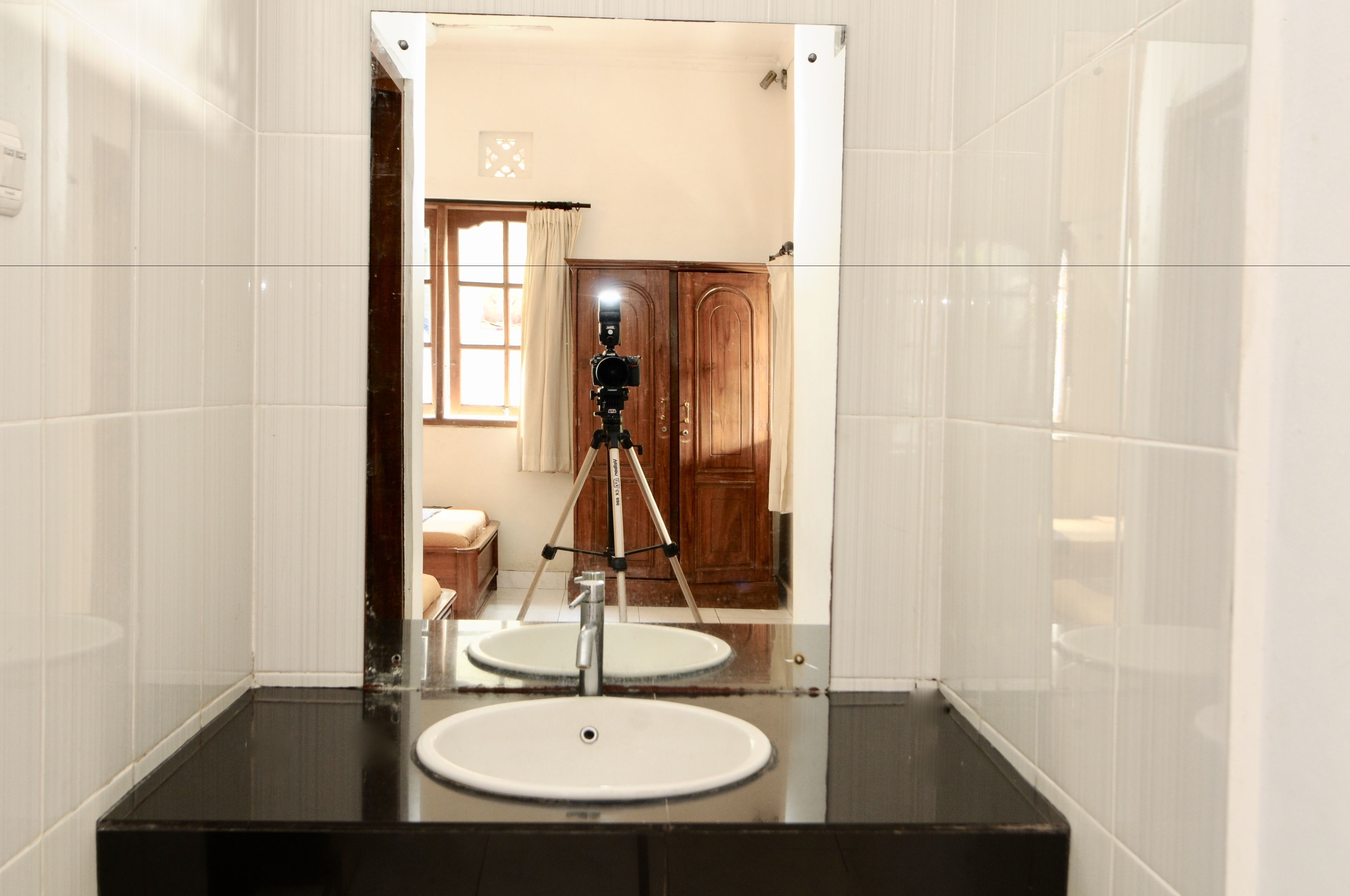 A bathroom with a large mirror, a sink, and a camera on a tripod in the background.