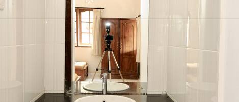 A bathroom with a large mirror, a sink, and a camera on a tripod in the background.