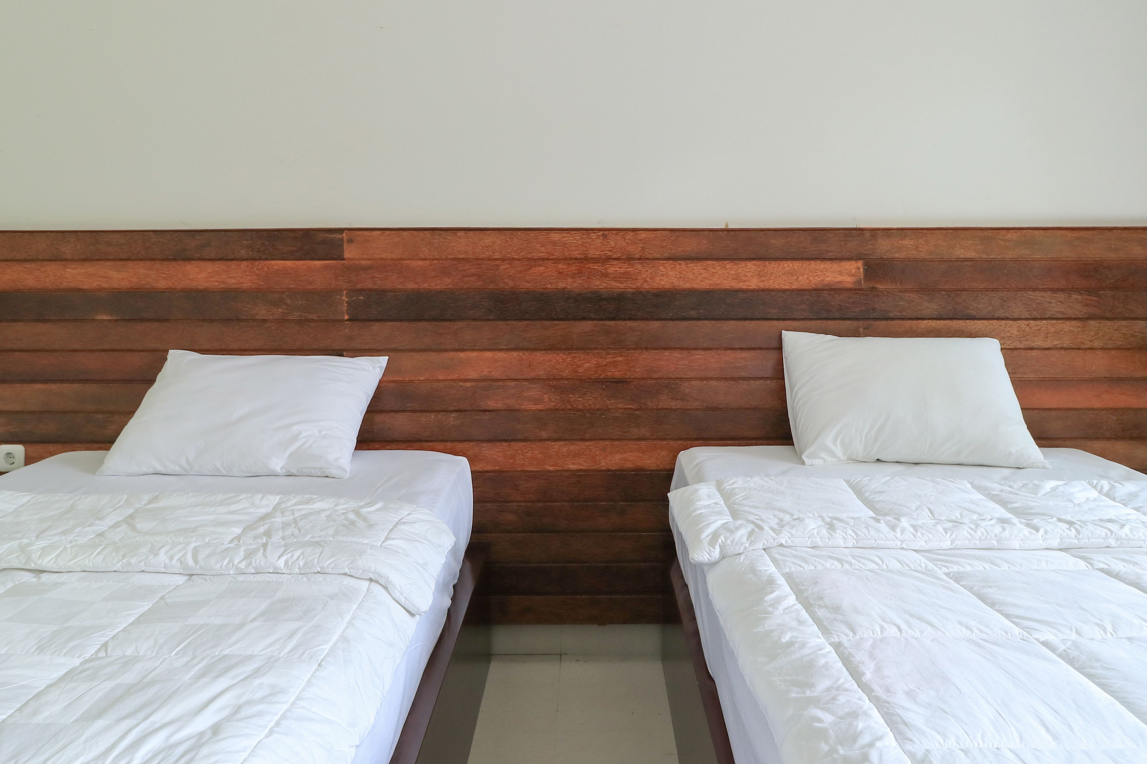Une chambre avec deux lits, chacun doté de draps et d’oreillers blancs, adossés à une tête de lit en bois.