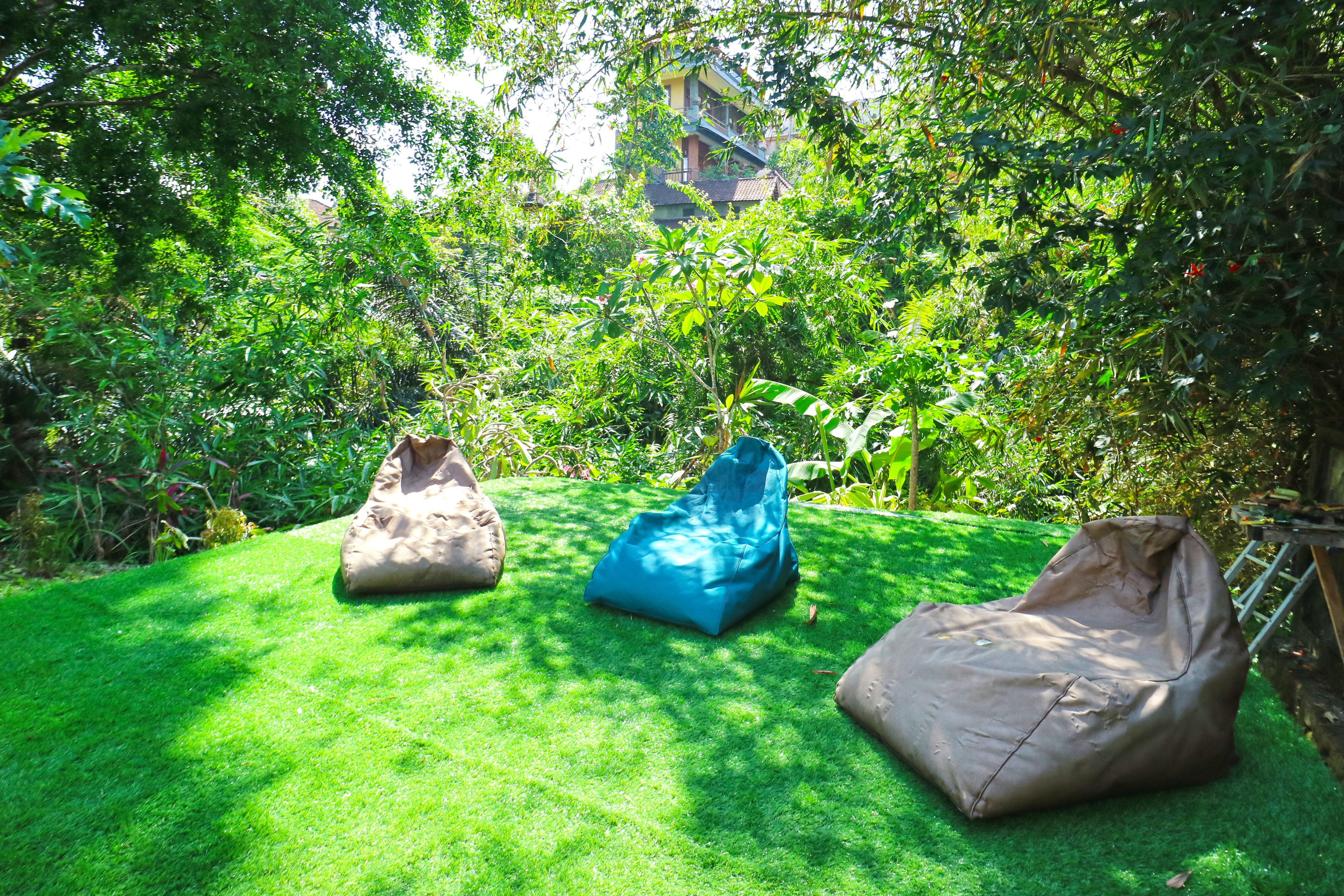 Un espace extérieur aménagé avec trois fauteuils en forme de sac de haricots, installé sur une pelouse bien entretenue, entouré d’une végétation luxuriante et avec un bâtiment en arrière-plan.