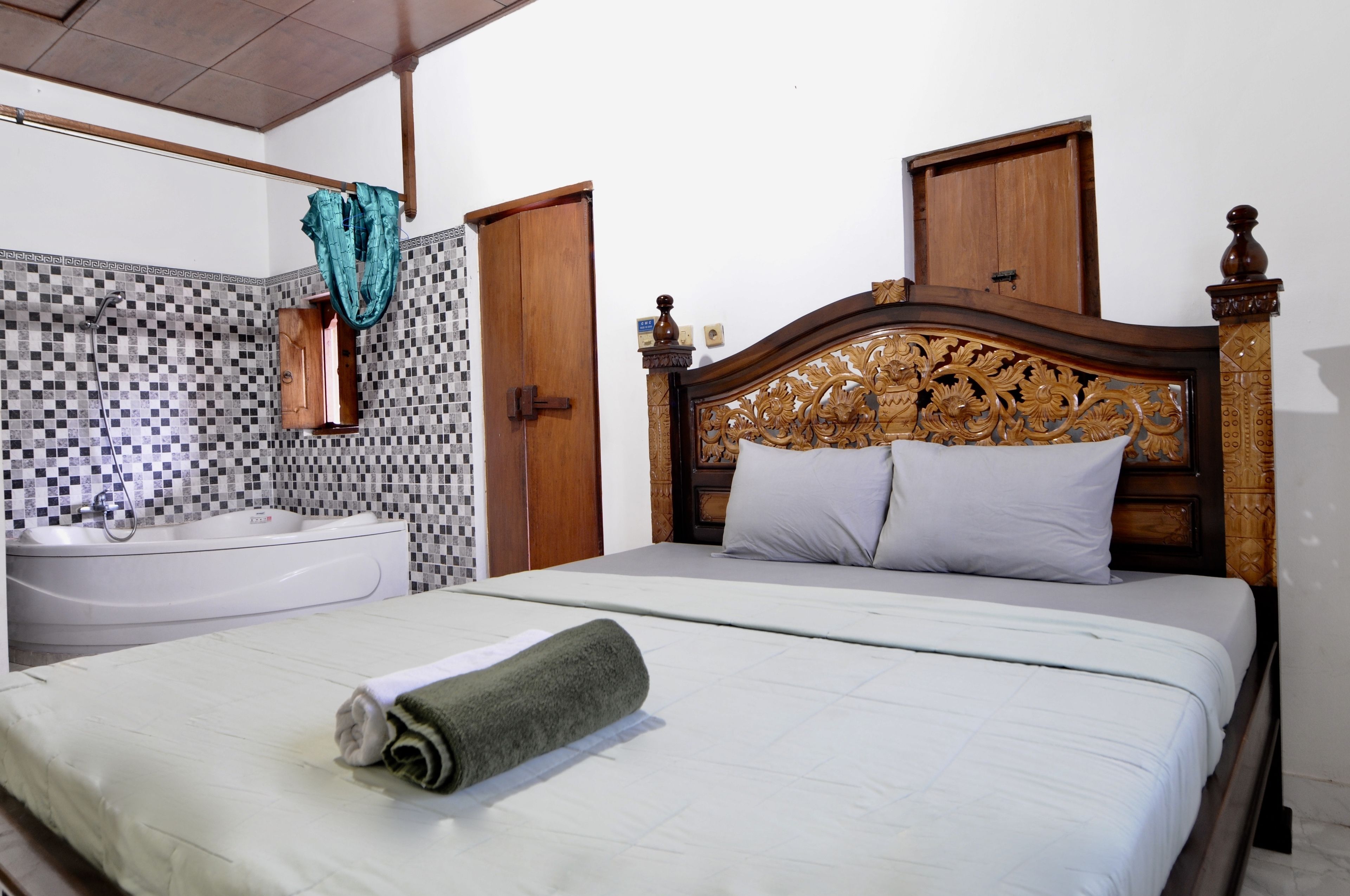 Une chambre d’hôtel avec un lit, une salle de bain comprenant un lavabo et un miroir, et une tête de lit en bois.