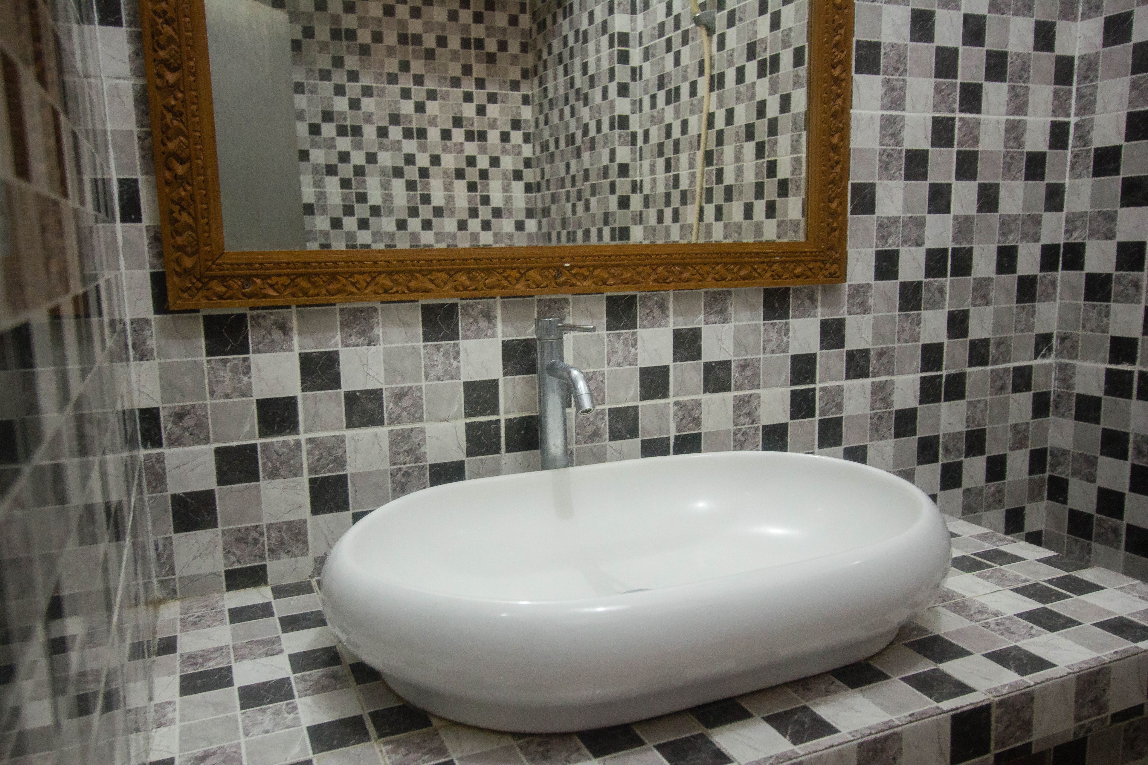 A bathroom with a white sink, a mirror with an ornate frame, and checkered tile walls.