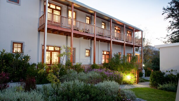 A multi-story building with balconies, a garden with various plants, and a well-lit entrance. - The Queen of Calitzdorp (Calitzdorp)