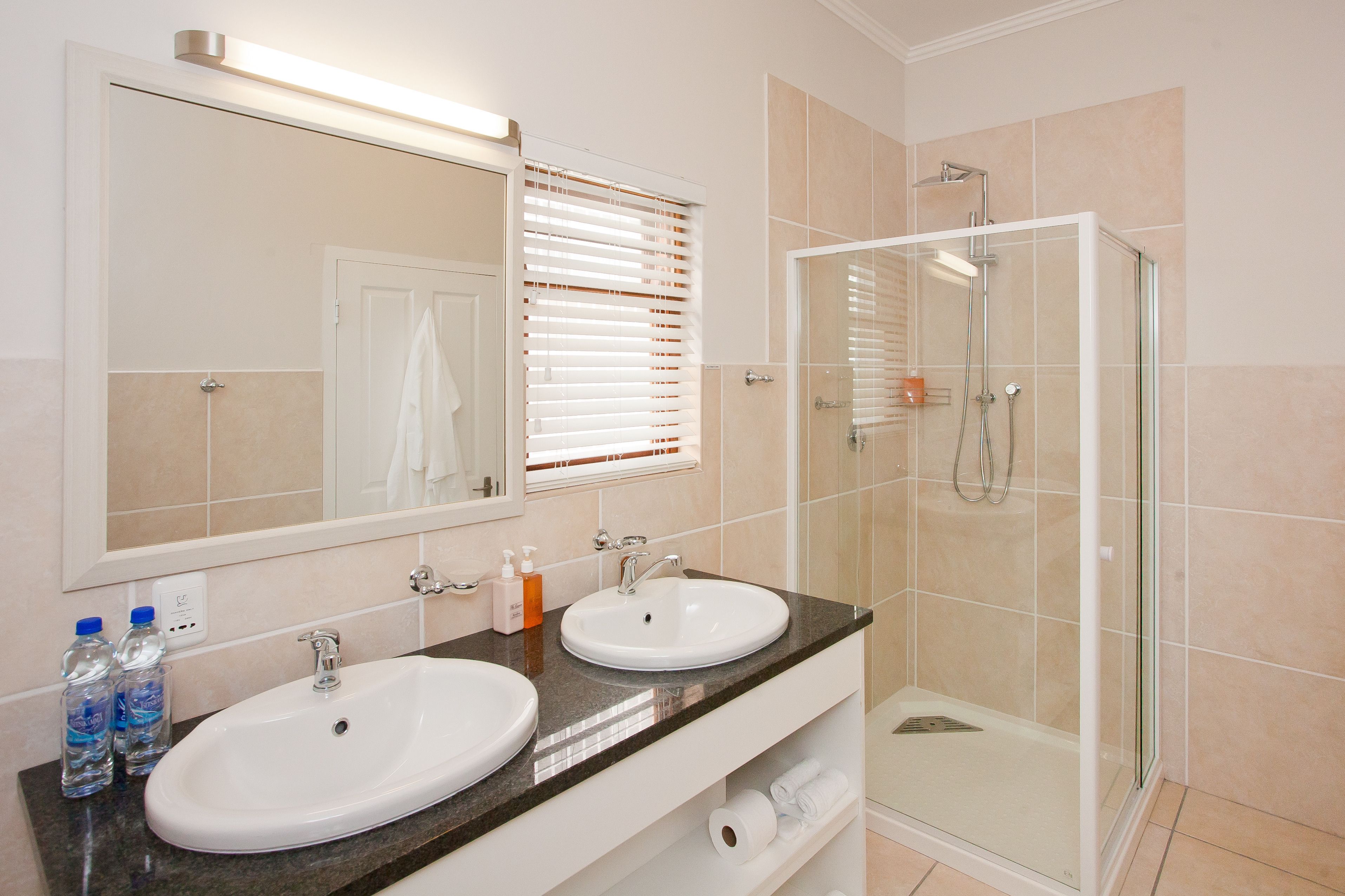 Een badkamer met twee wasbakken, een spiegel, een douche en een douchecabine met glazen wanden.