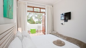 A hotel room with a bed, a TV mounted on the wall, a window with curtains, and a view of the outdoors. - The Queen of Calitzdorp (Calitzdorp)