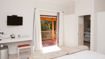 Un dormitorio con cama, escritorio con televisor, baño y balcón con vistas a zonas verdes.