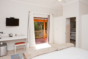 A bedroom with a bed, a desk with a TV, a bathroom, and a balcony with a view of greenery.