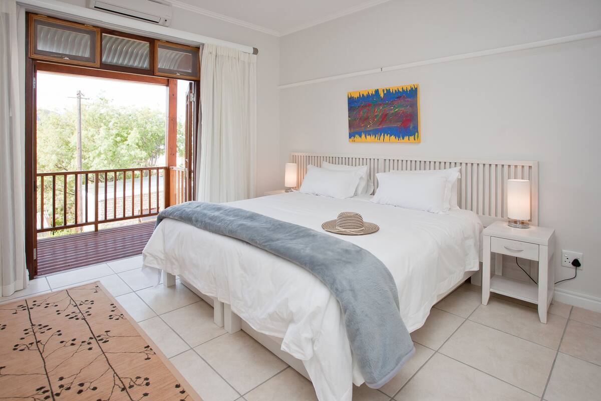 A bedroom with a bed, bedside tables, a window with curtains, and a painting on the wall.